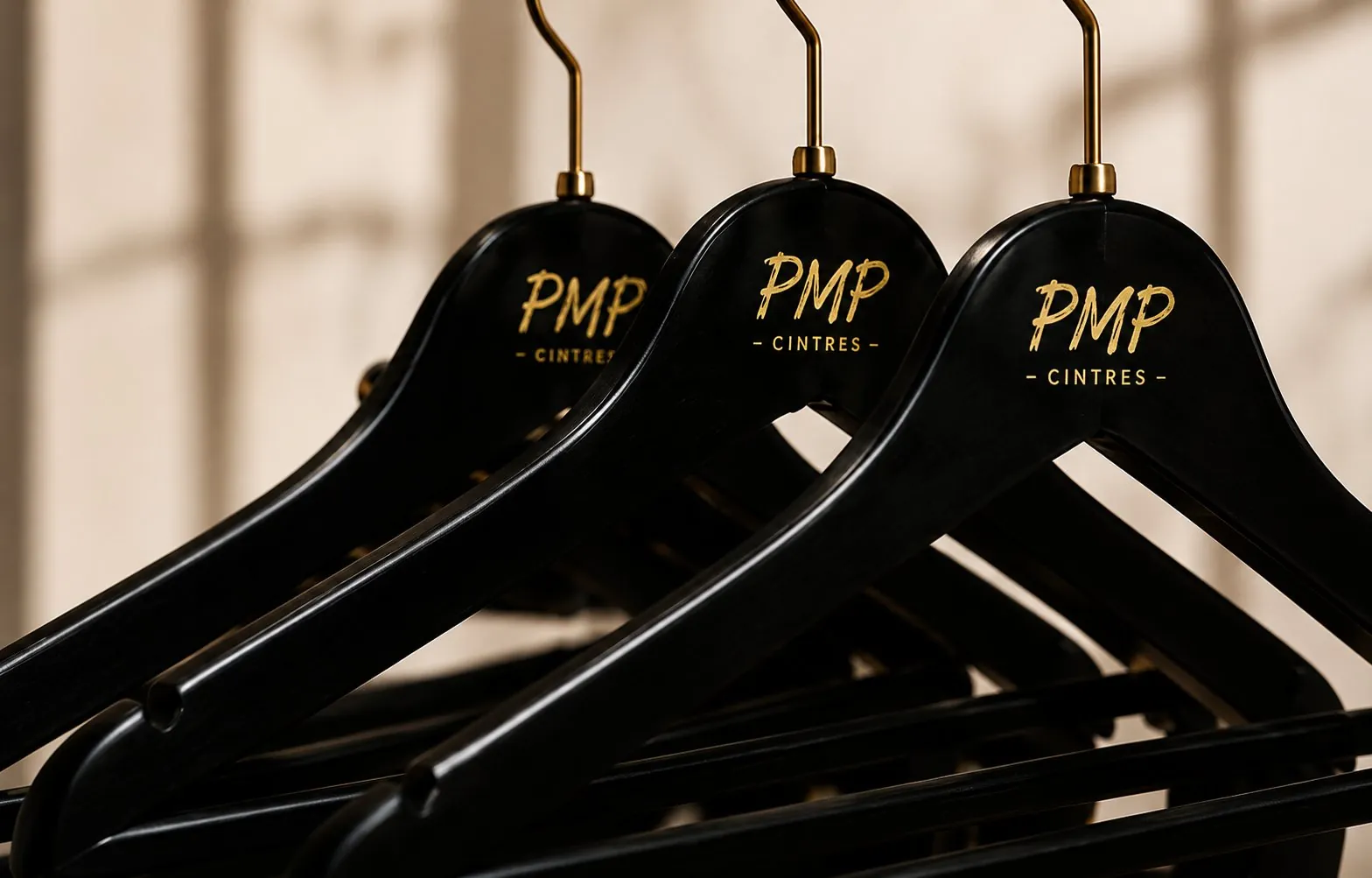 Trois cintres noirs brillants personnalisés avec logo PMP Cintres doré